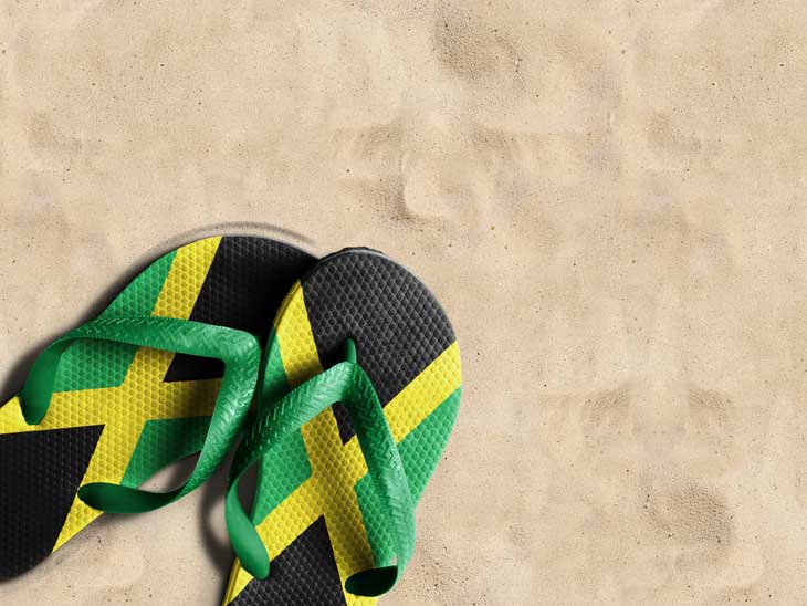 Slippers in the Jamaican colors on beach sand.